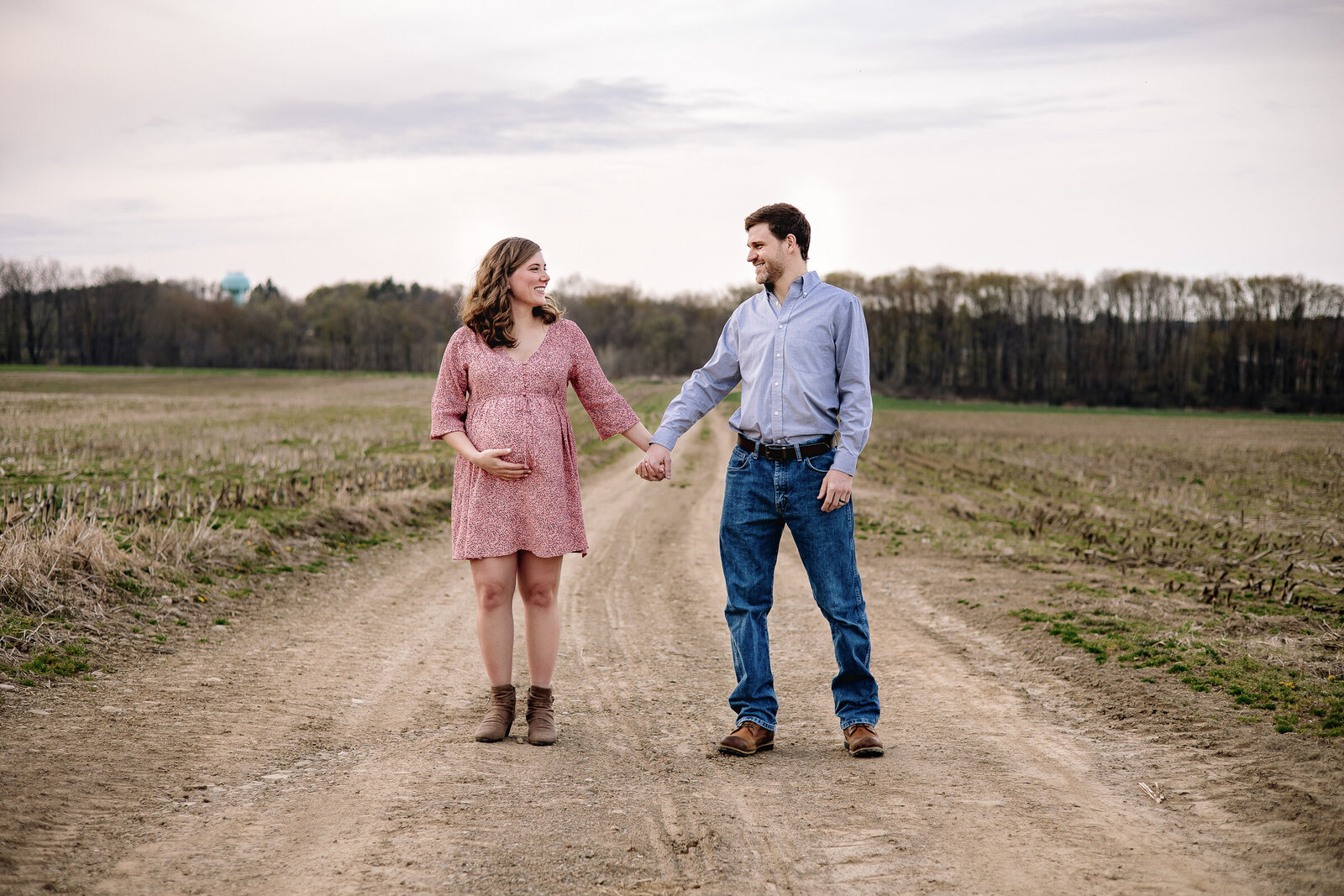 Expectant parents stand hand in hand on a country road