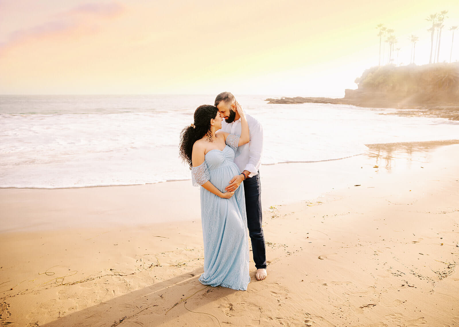 Couple standing on beach embraced during maternity session by Ashley Nicole.