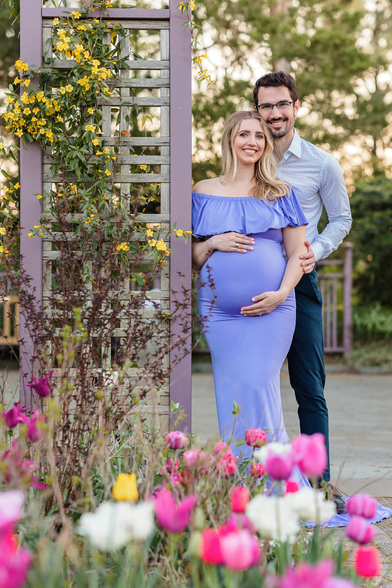 A couple expecting their first baby posing against a trellis at Greenspring Gardens.