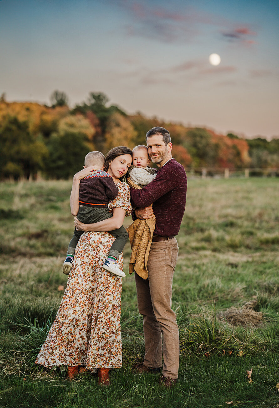 family with two sons snuggles together for pictures under autumn moon