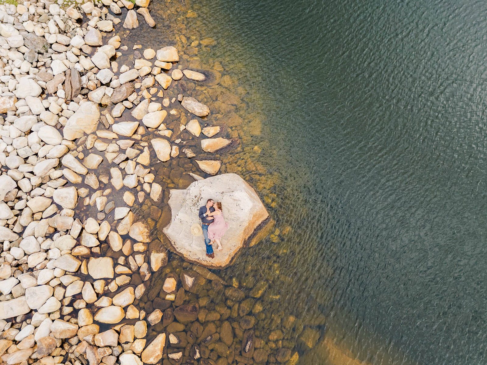 Couple cuddling on a rock surrounded by serene waters and rocky shores at Snowy Range Mountains in Laramie Wyoming, captured from above with a drone.