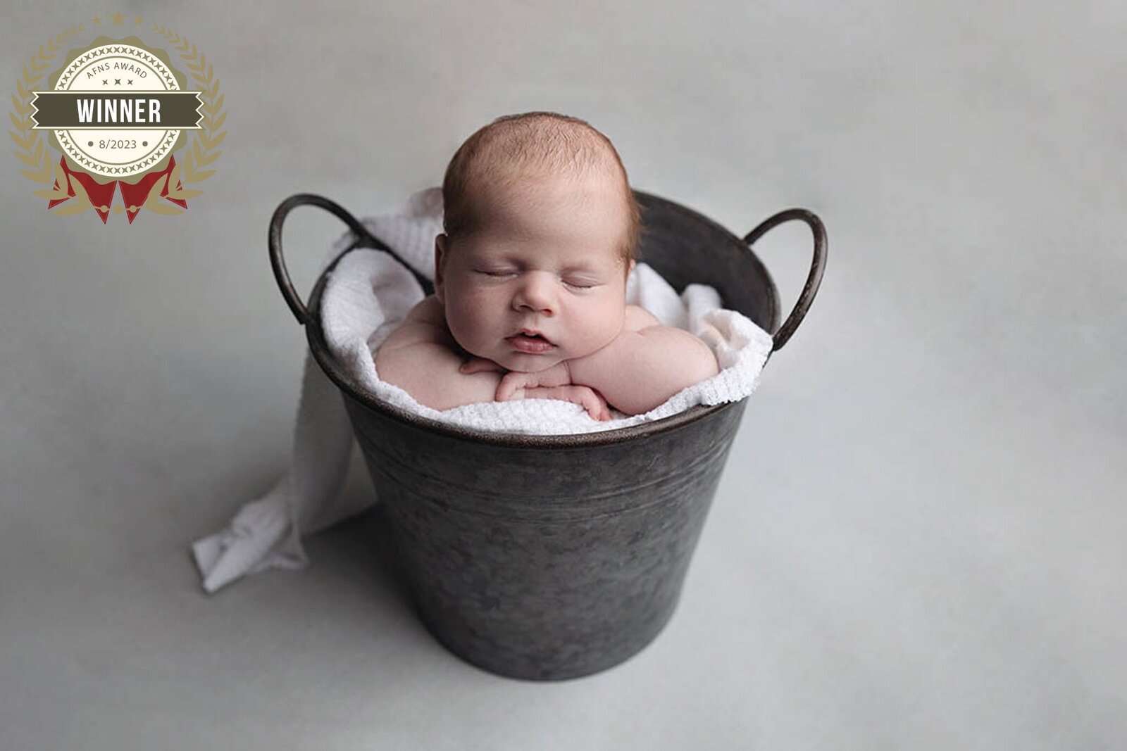 Newborn baby boy sleeps in metal bucket with hands under chin for his newborn pictures in Greensburg.