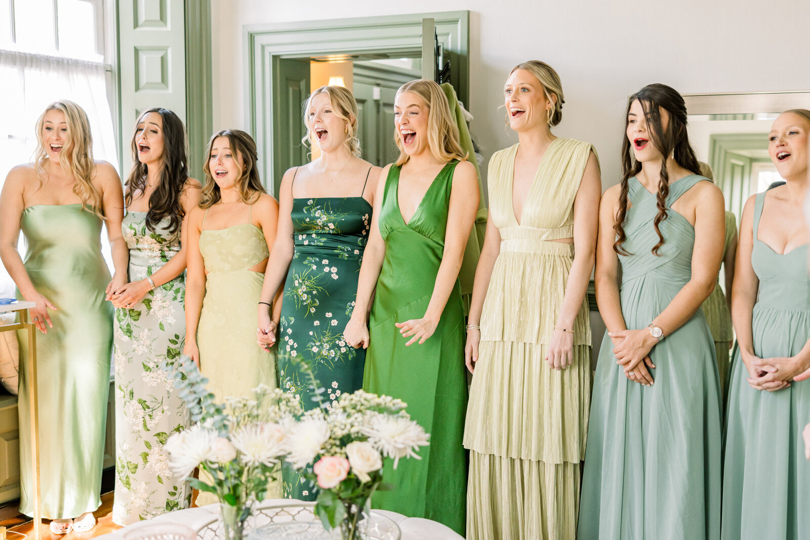 Bride’s emotional first look with bridesmaids dressed in beautiful floral prints with green tones, capturing a heartfelt and joyful wedding moment.