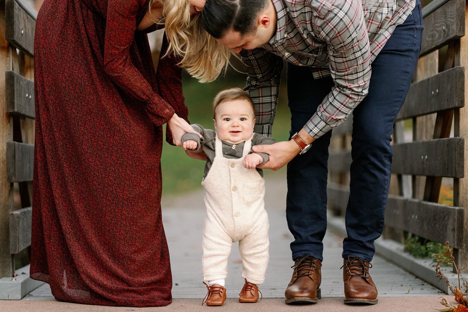 baby boy in overalls with mom and dad on bridge