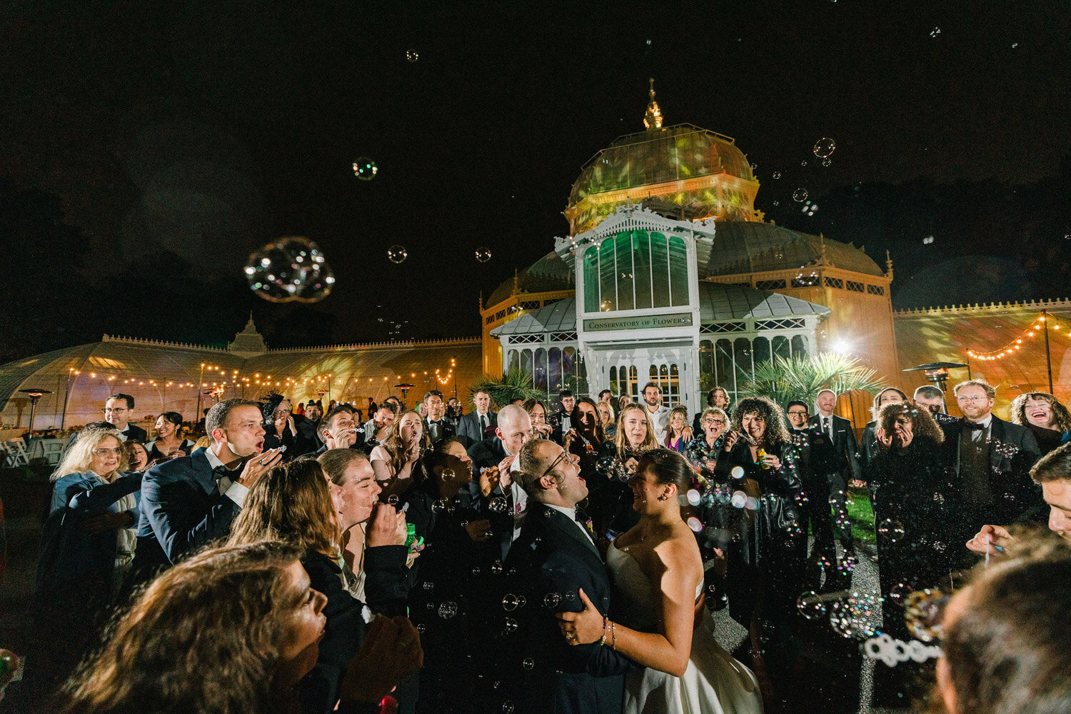 Wedding guests blowing bubbles at couple outside venue