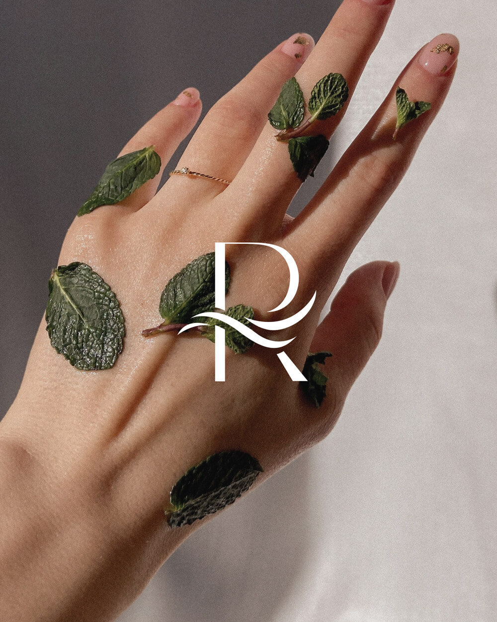 a branded lettermark of the letter R overlayed on an image of a hand with herbs on it