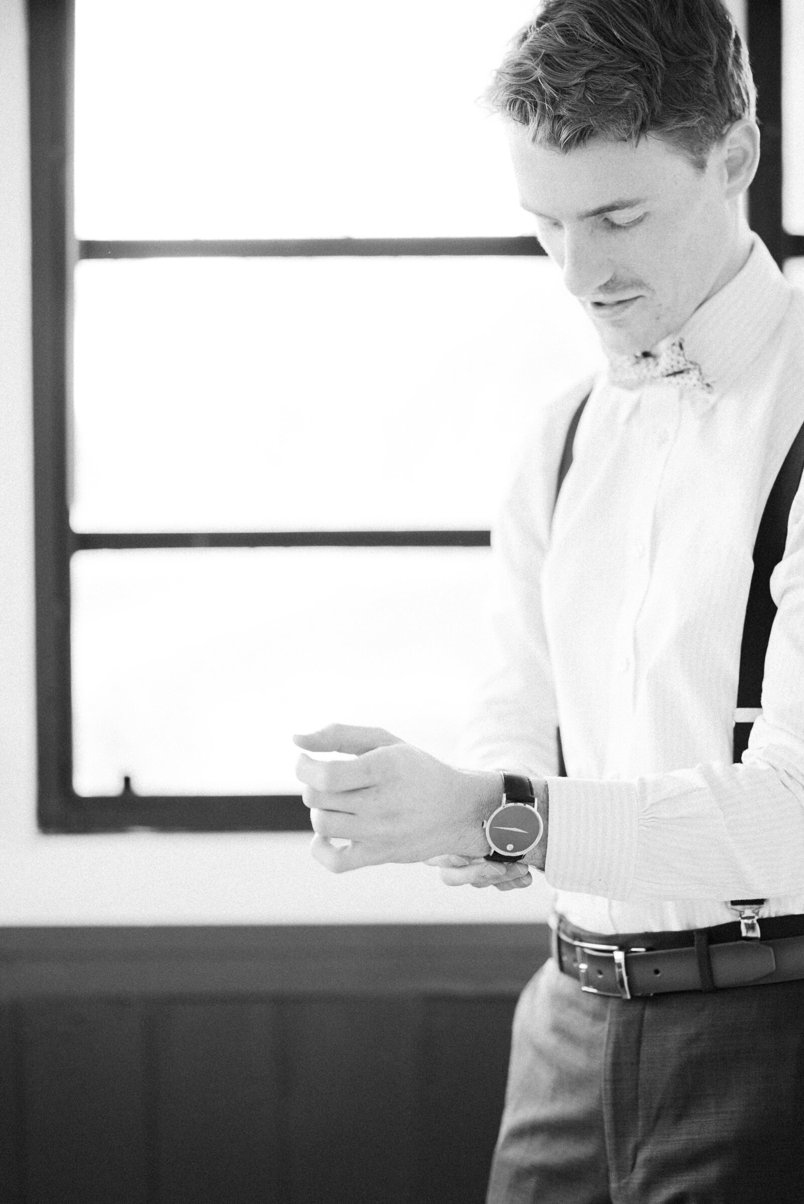 Groom getting ready for his wedding, putting his watch on his wrist while looking down at it.