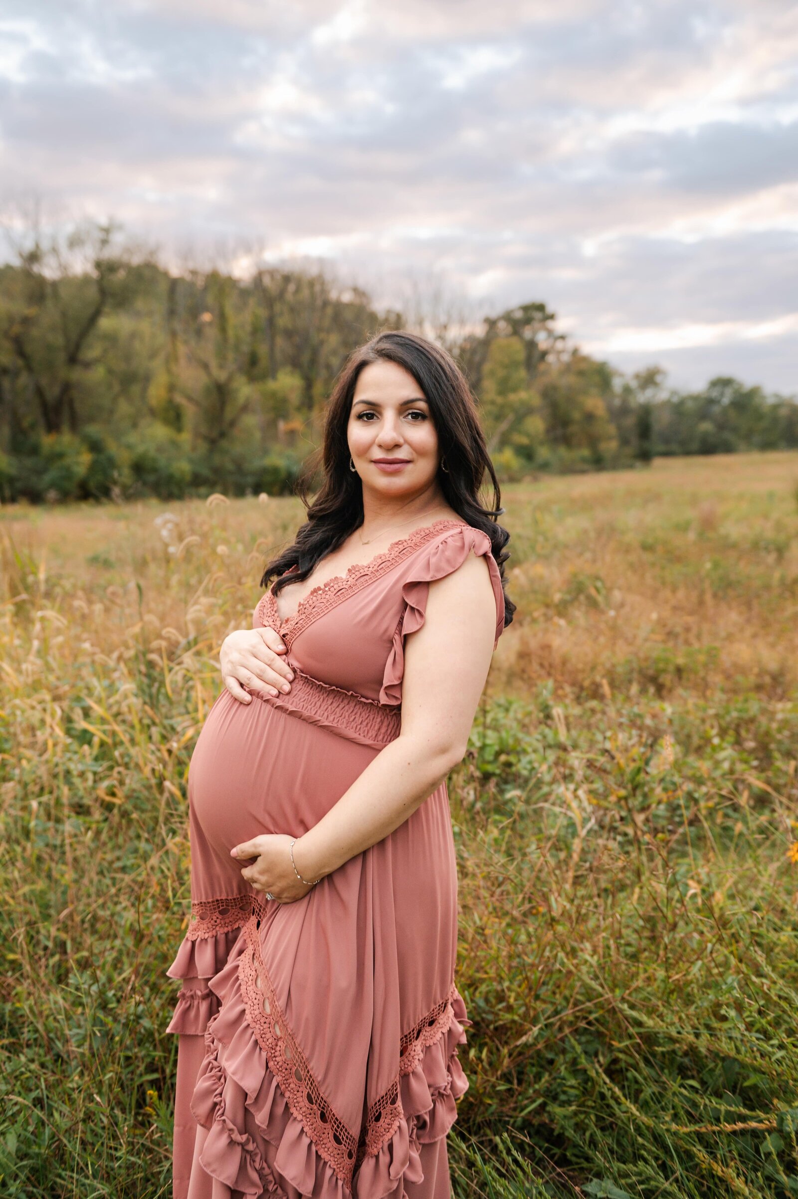 woman in blush dress holding her belly smiling at camera