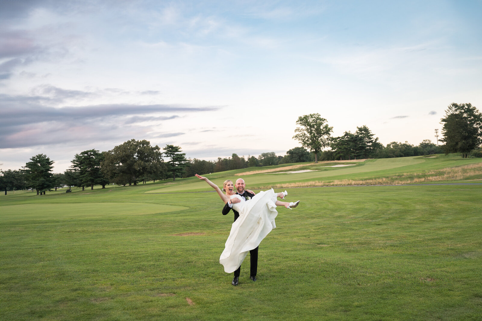 A bride and groom at Riverton Country Club.  Groom is holding the bride in the air.