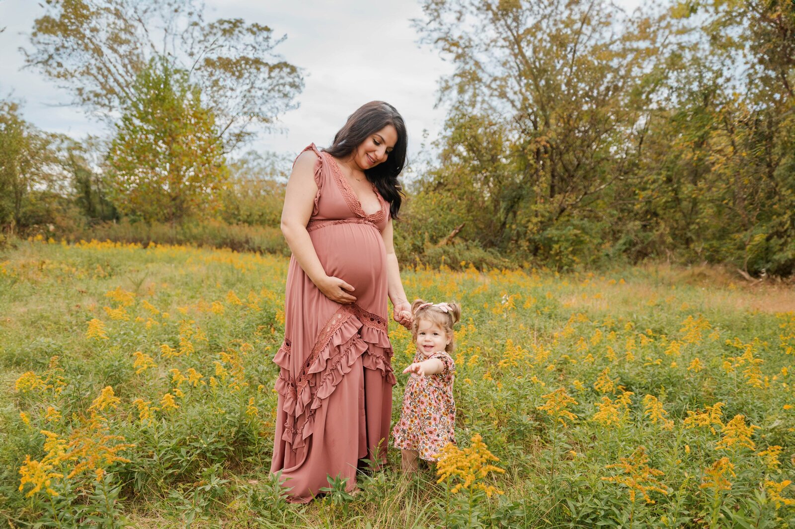 mom holding toddlers hand while getting pregnancy photos