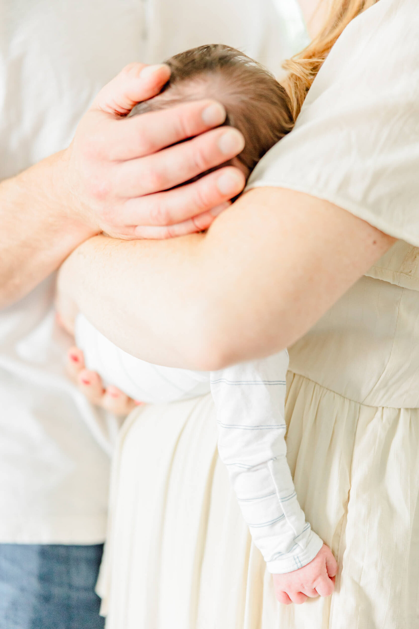 Close up of newborn in mom's arms with dad's hand feeling the baby's head