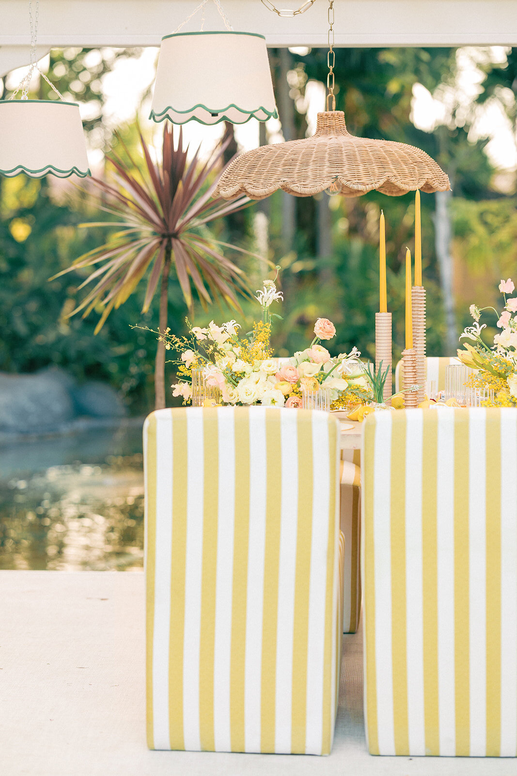 Yellow and white striped chairs with rattan pendant hang over tablescape with yellow and orange flowers and yellow taper candles