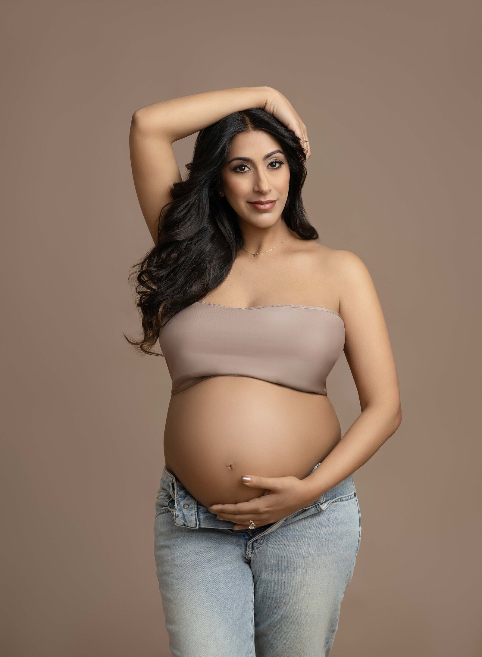 Mom holding baby bump and other hand resting on head, smiling at camera. Photo taken at Atlanta Maternity photo studio in Woodstock, GA.
