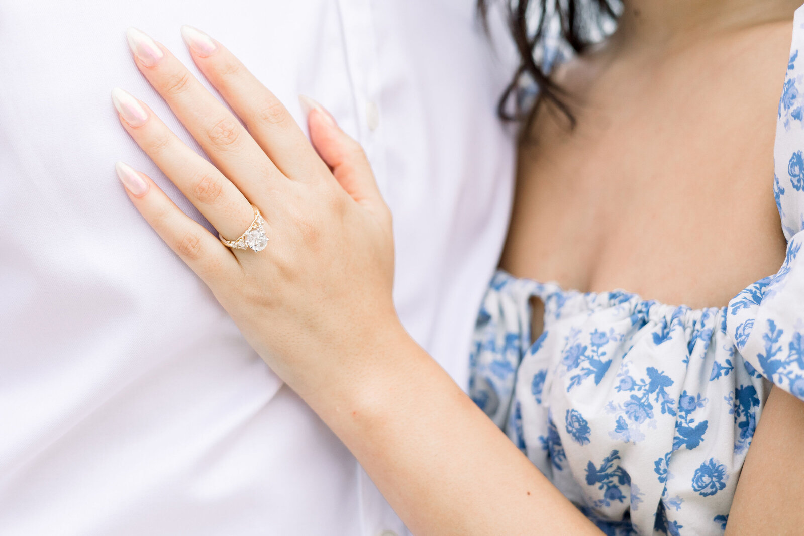 detail shot of engagement ring as woman holds her hand on her fiances chest for beach engagement pictures