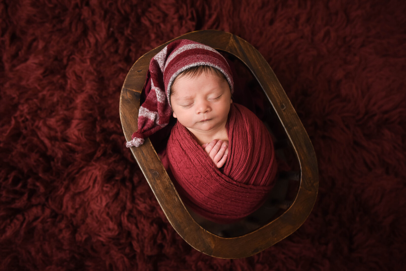 newborn wrapped in red blanket laying in wooden dough bowl for photo session