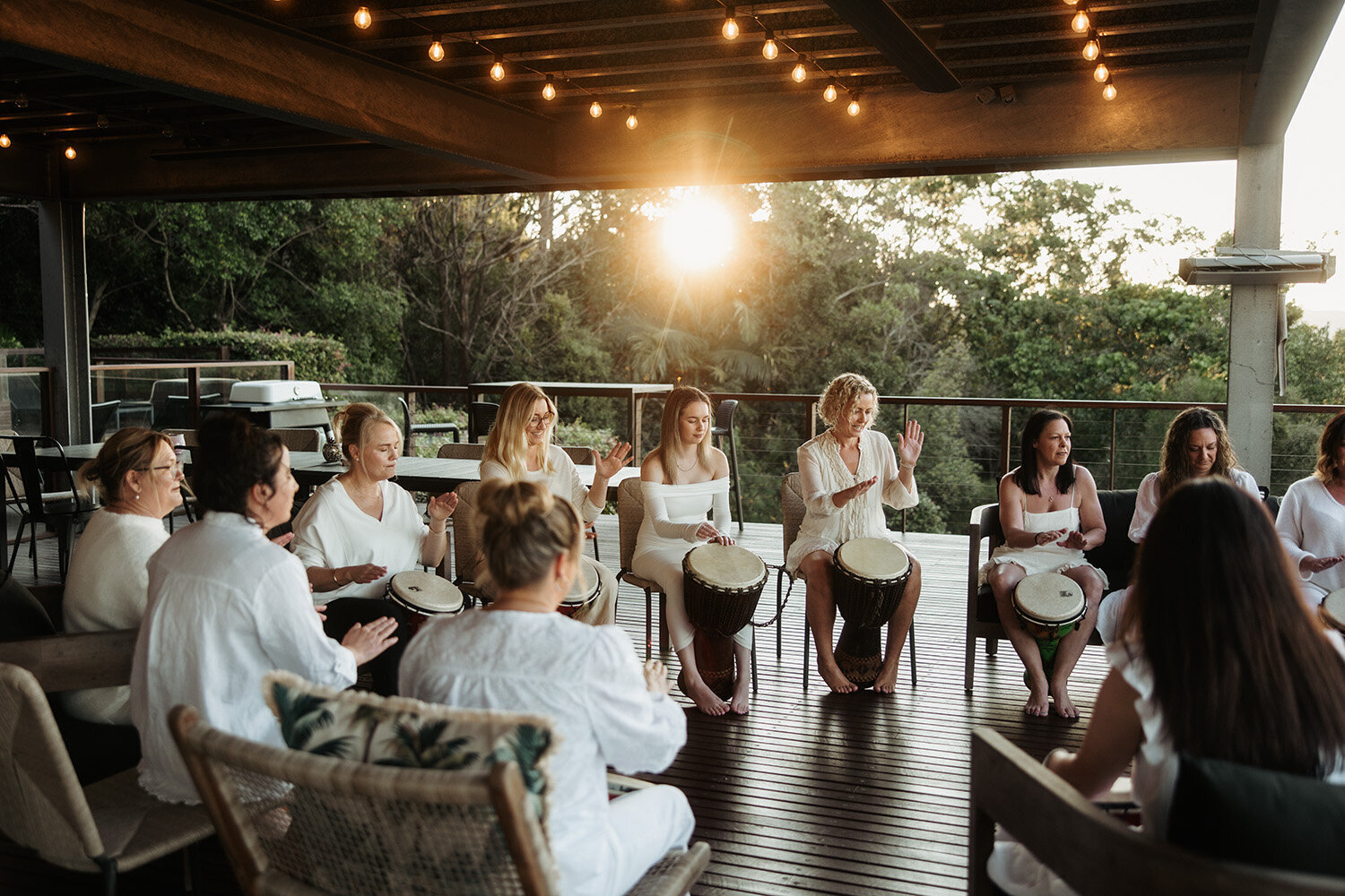 Women participating in a drum circle on a wooden deck during a wellness retreat, photographed by Sunshine Coast event photographer.