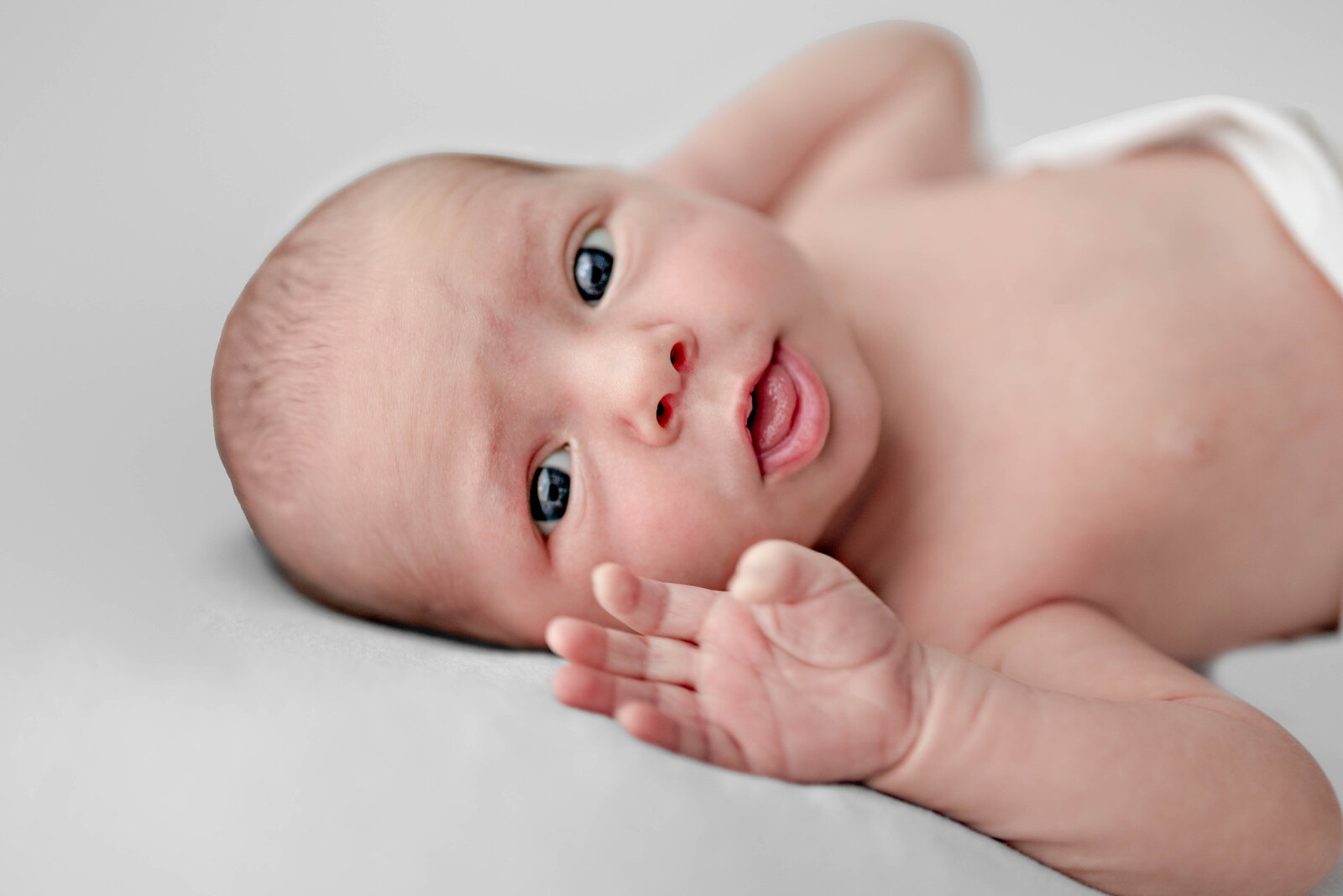 A newborn  baby looks at the camera and appears to wave  during his newborn photoshoot at a studio in Huntsville Alabama