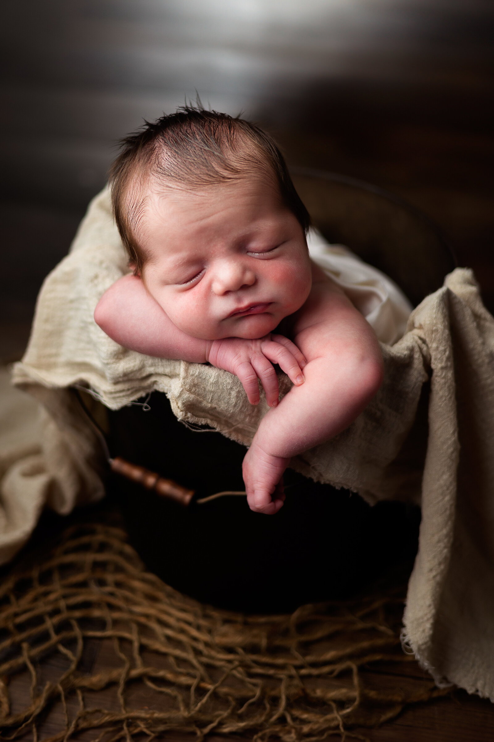 Newborn baby boy sleeping soundly while posed in a  brown bucket