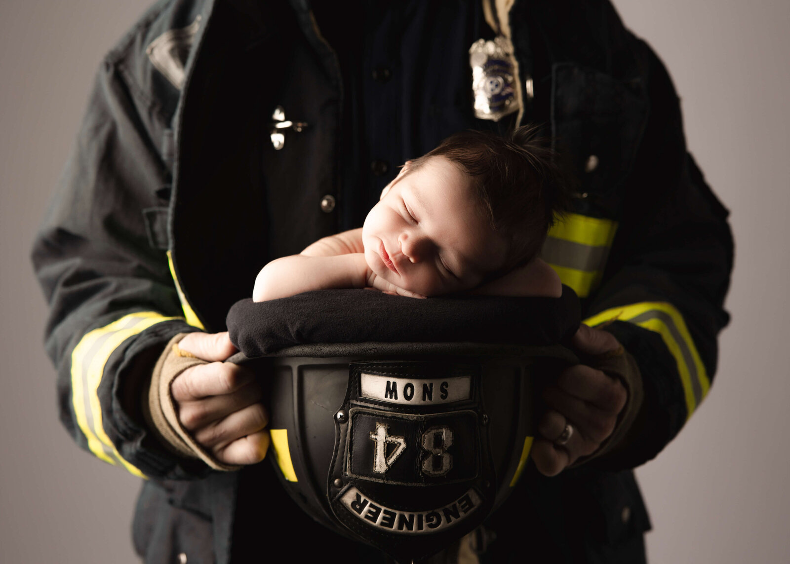 Newborn posed in dads fire fighter helmet in studio by Ashley Nicole.