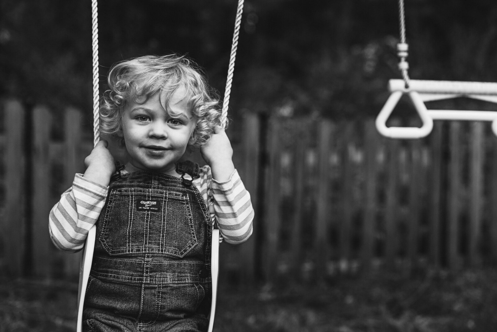 A young boy swings in a playyard playground for a black and white photo.