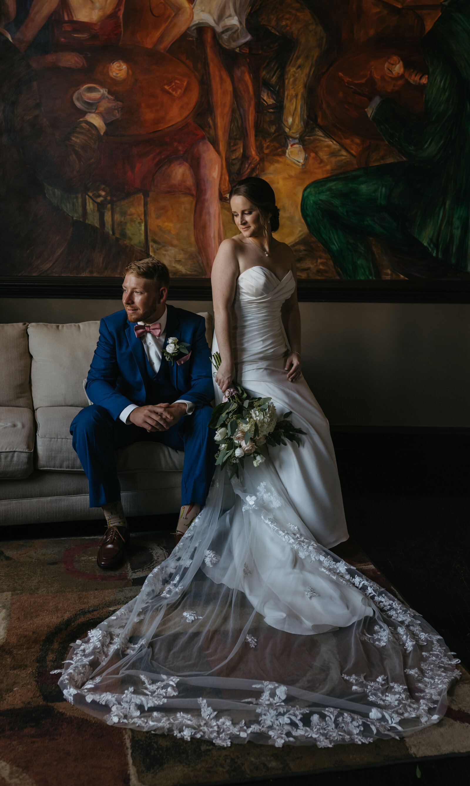 A bride and groom sit in front of a large painting in a hotel