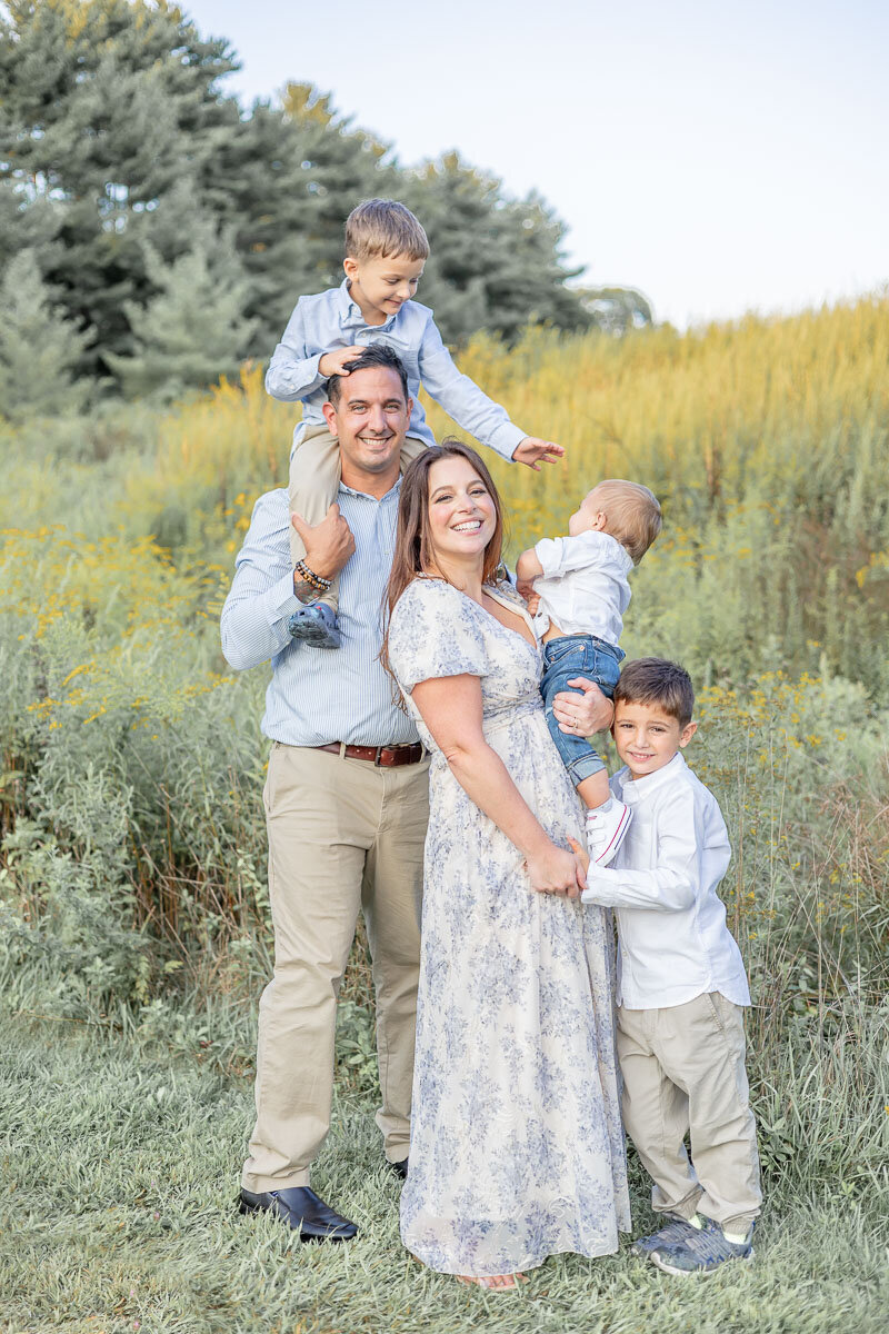 Golden hour family portrait in a wildflower field with three boys, showcasing a relaxed and joy-filled outdoor session by Nicole, a Connecticut and Westchester lifestyle family photographer.