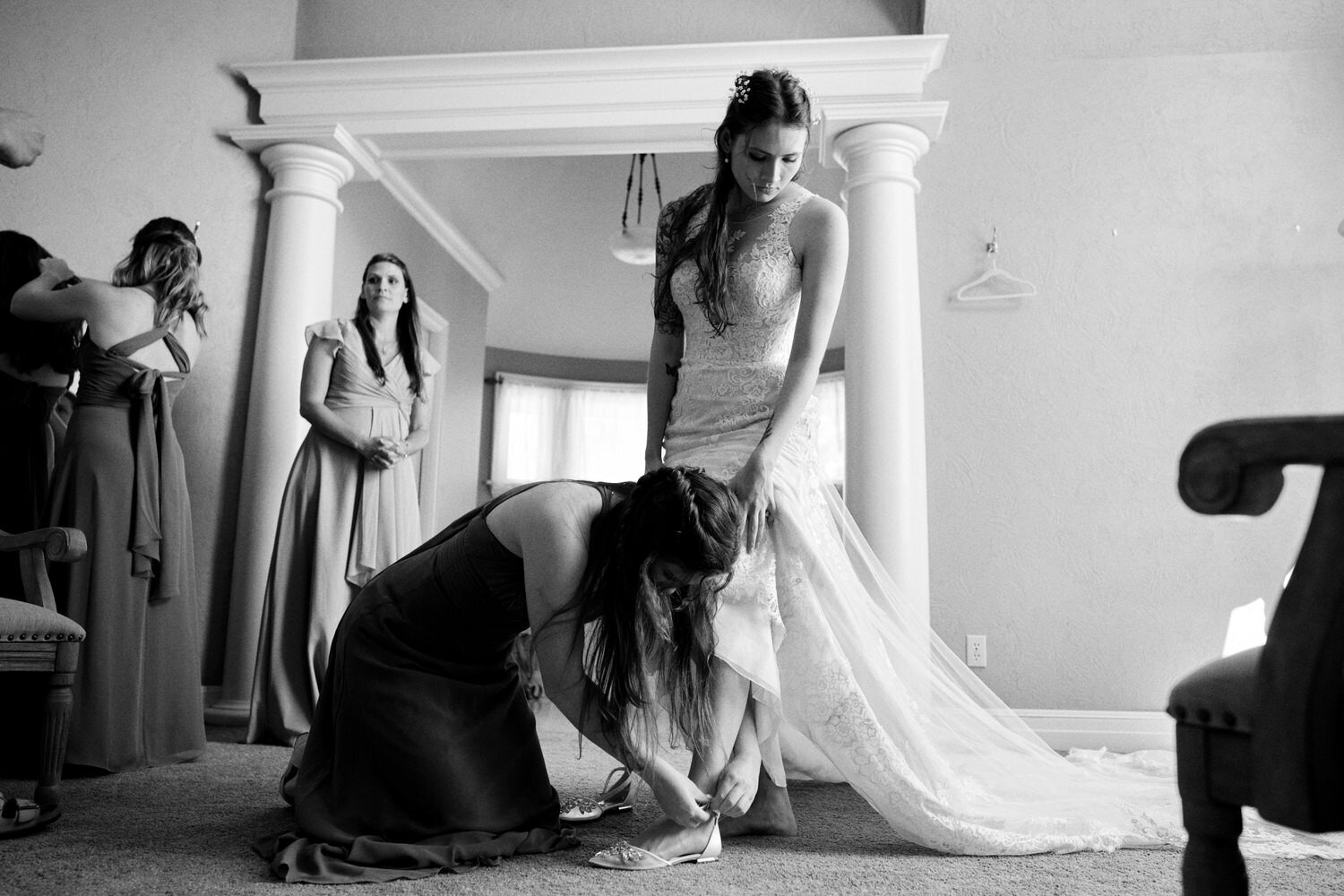 Bridesmaid helps the bride get her shoes on.
