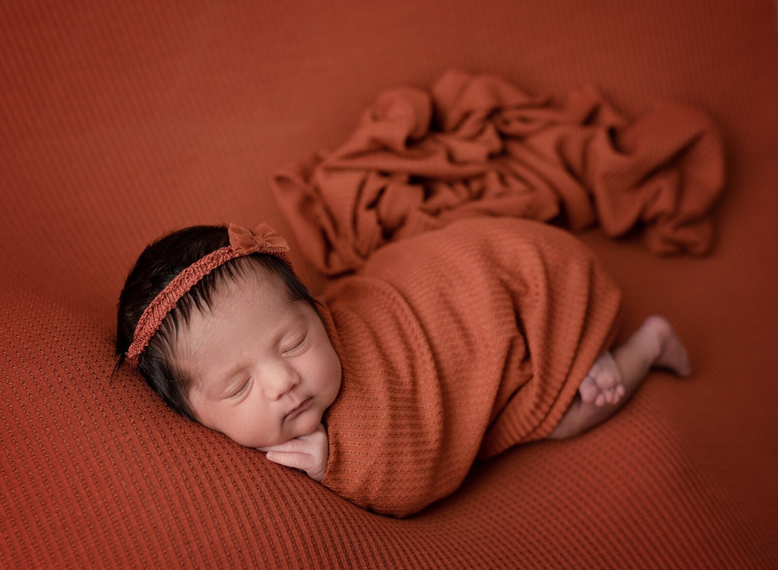 a baby girl sleeping on a burnt orange blanket and wrapped in a matching scarf
