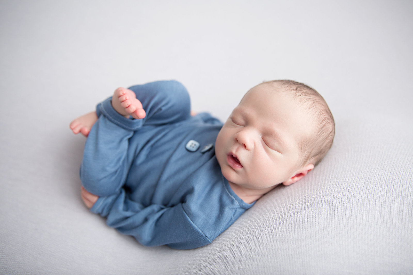 sleeping newborn baby wearing blue outfit on light grey fabric