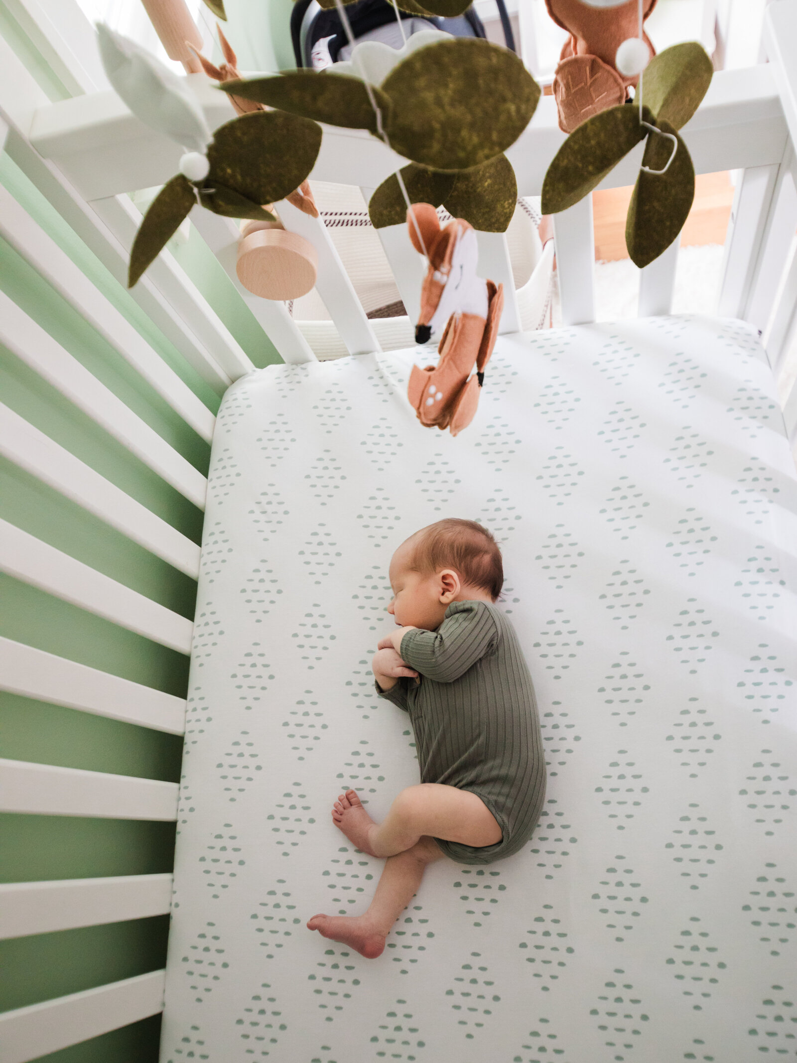 newborn baby boy in green onesie laying in crib