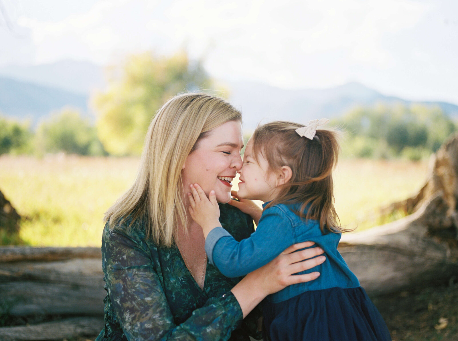 A blonde woman in a green dress receives a kiss from her toddler daughter