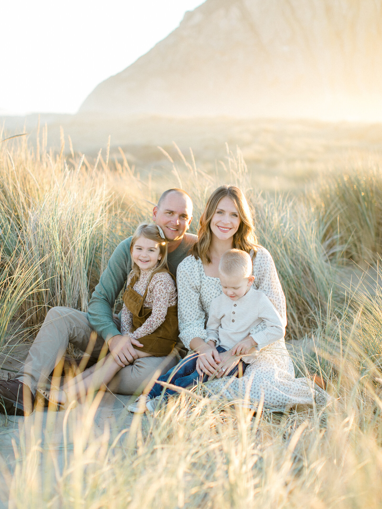 family of four sitting in the sand and grass and smiling