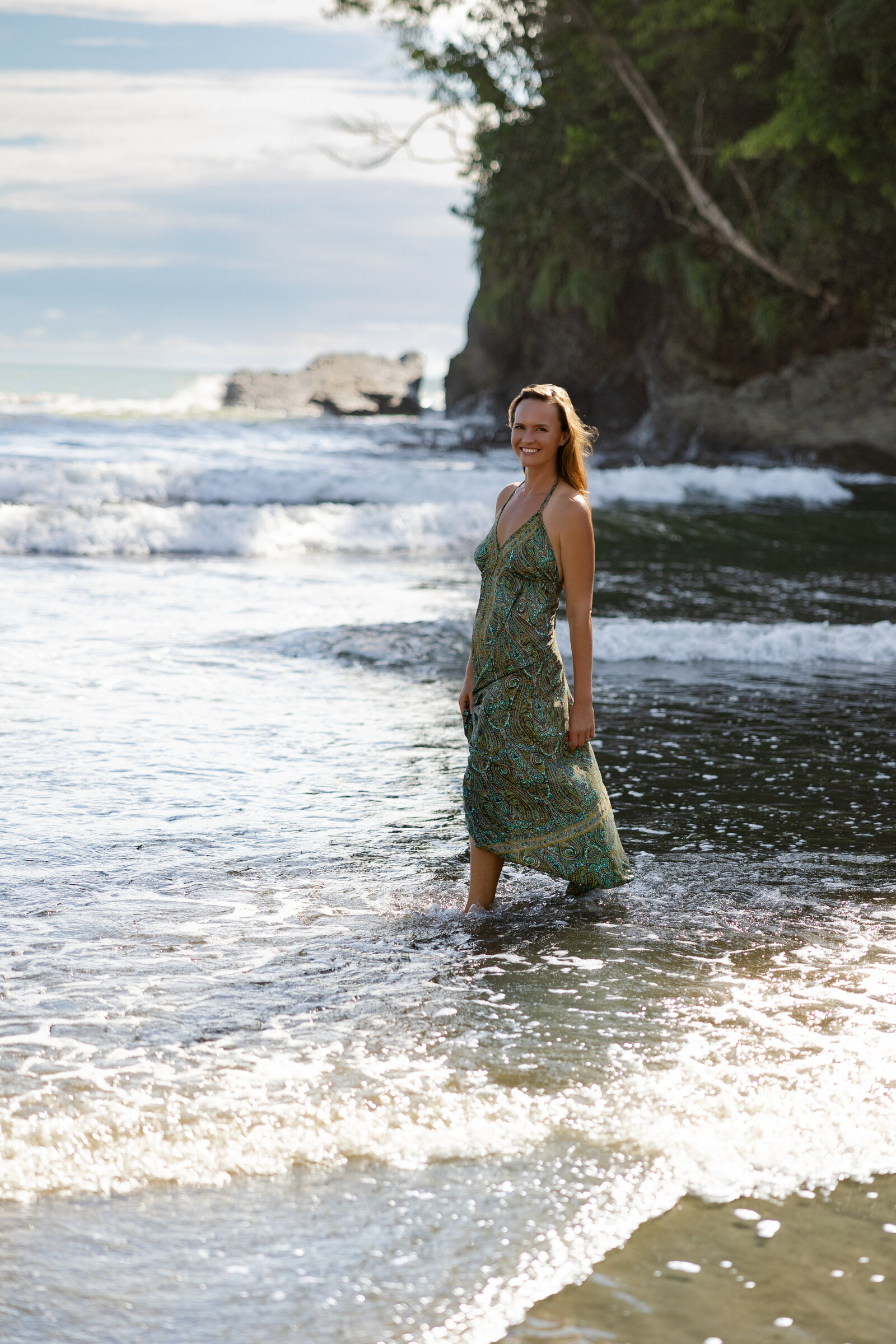 A woman walking on the shore with caves behind her