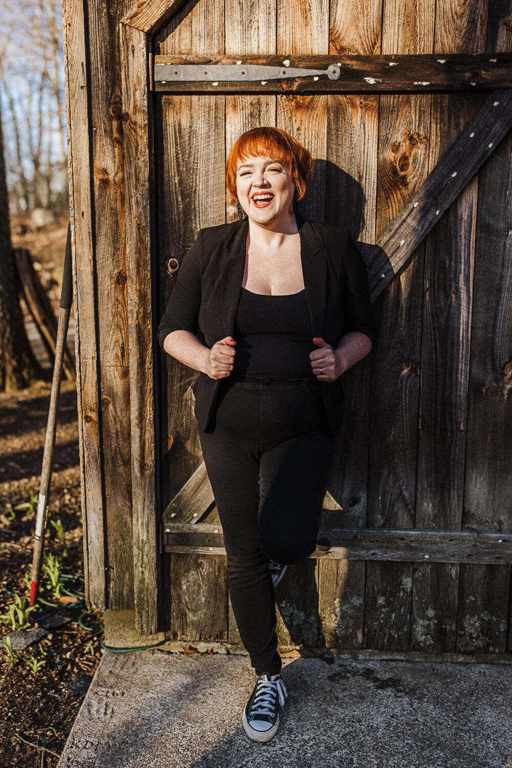 woman dressed in black laughs against barn wall