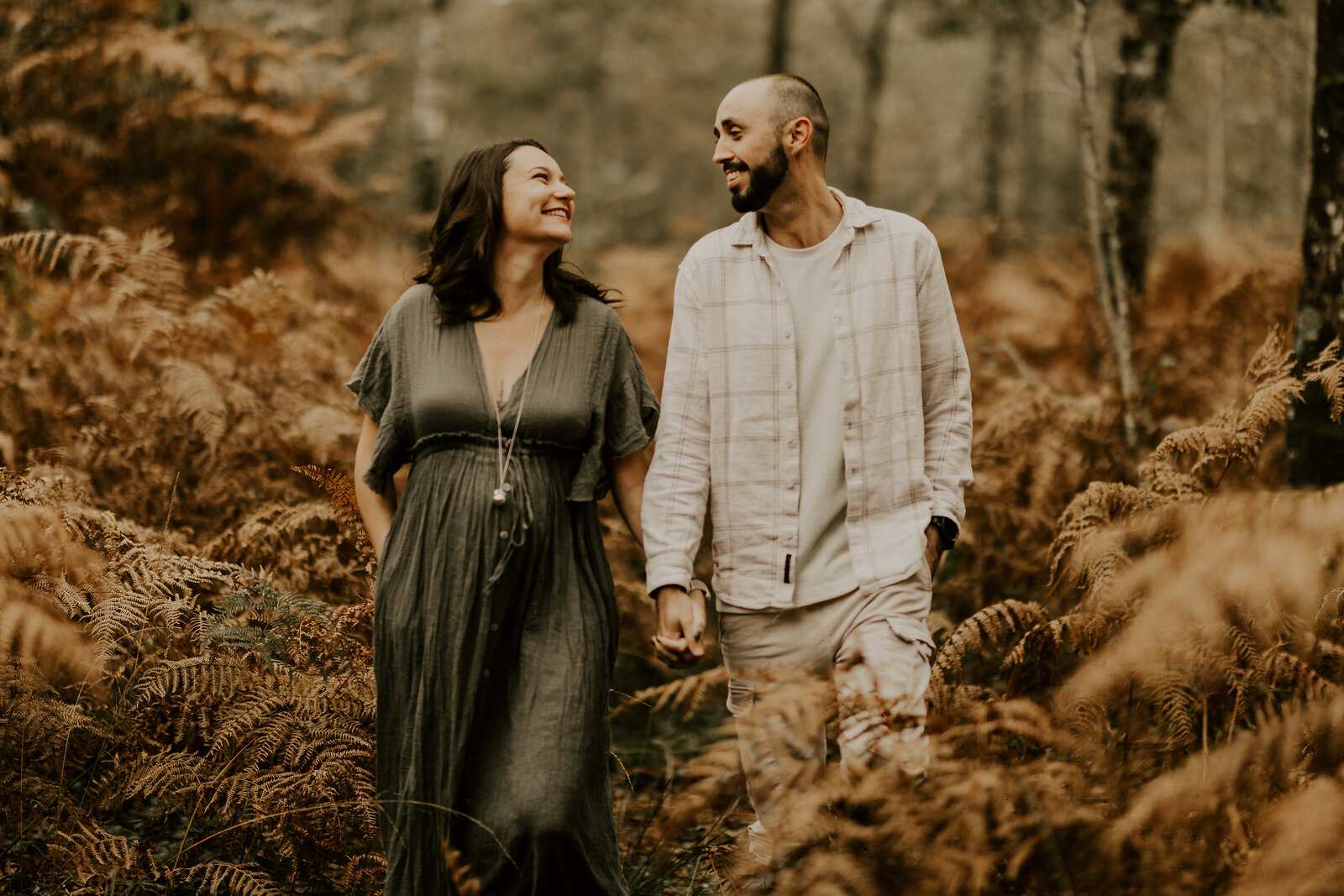 Couple en bord de mer, la femme enceinte en robe beige tient son ventre et pose tendrement contre son partenaire. Capturée par Laura, photographe en vendée.
