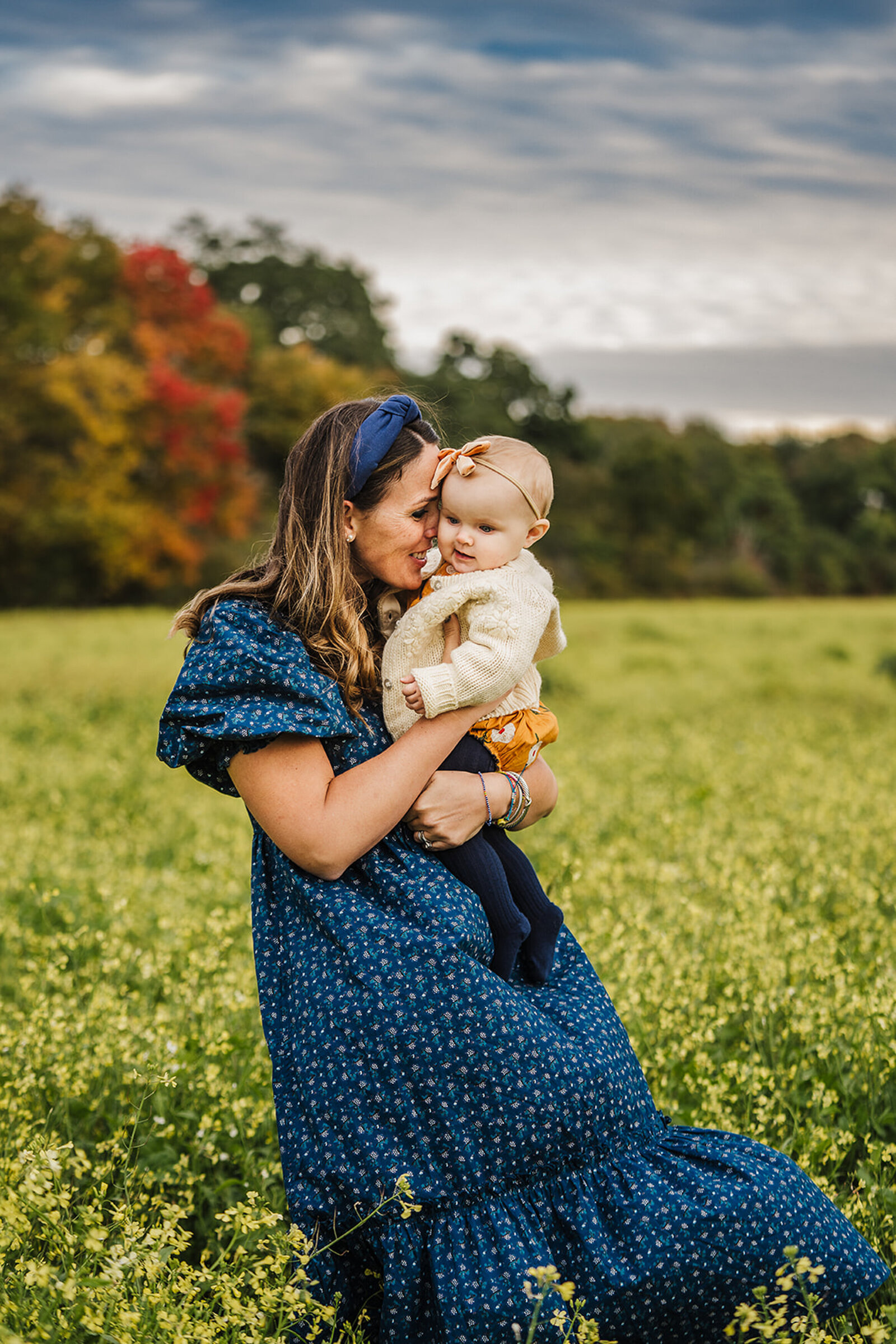 mom in blue dress snuggles baby in field of yellow flowers