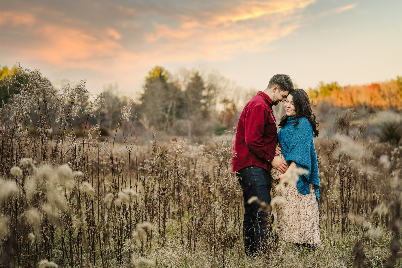 pregnant couple in field of dead grass at sunset