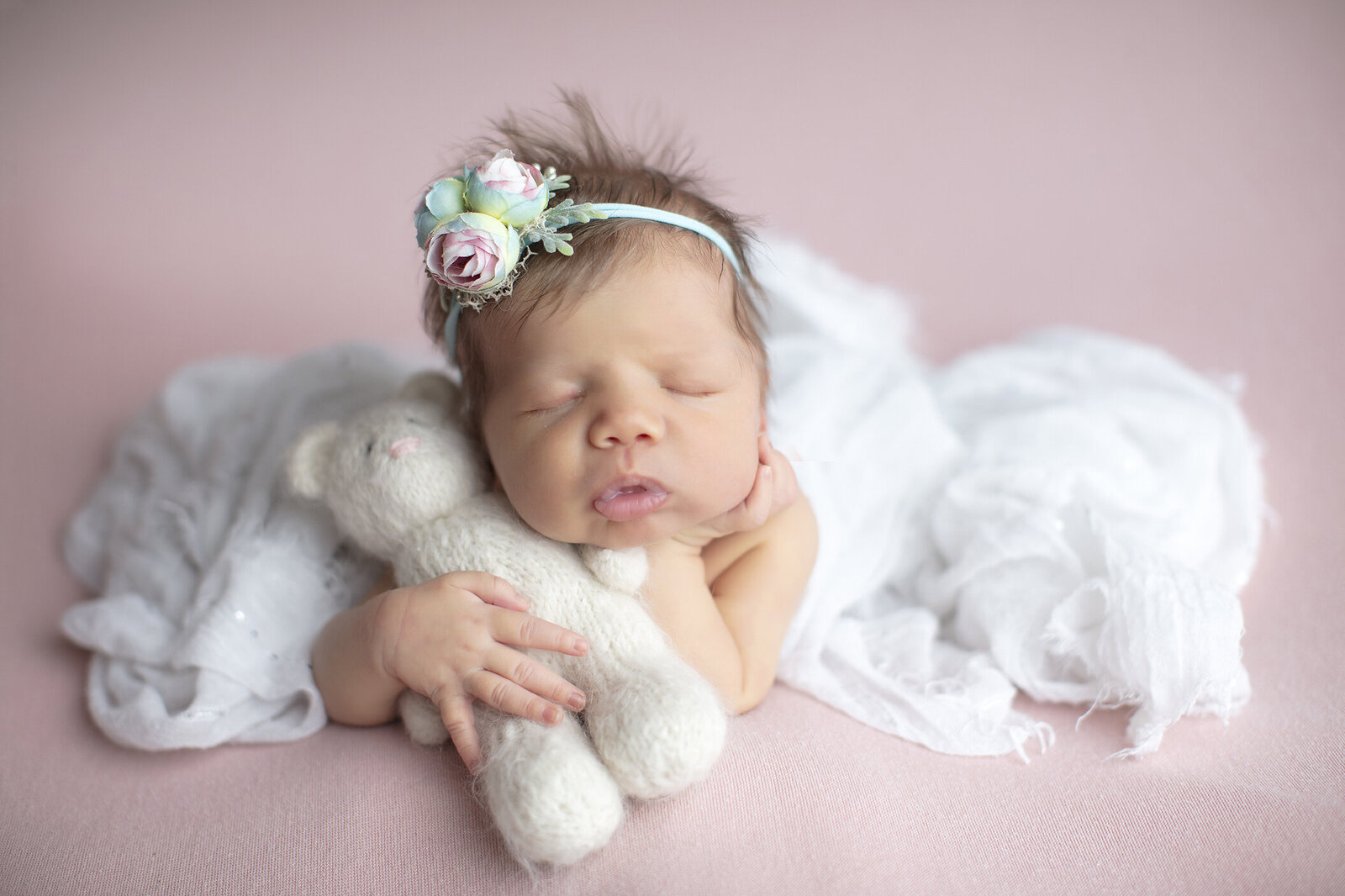 Newborn girl with teddy bear on pink fabric.