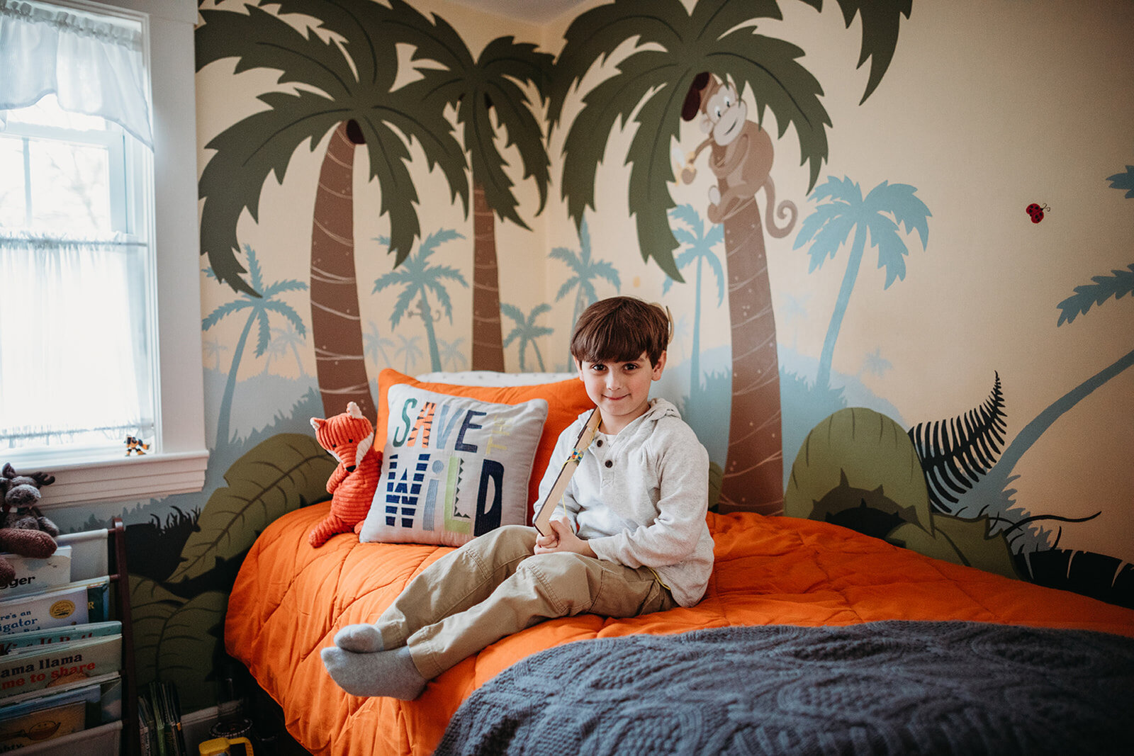 boy sits on bed in jungle bedroom