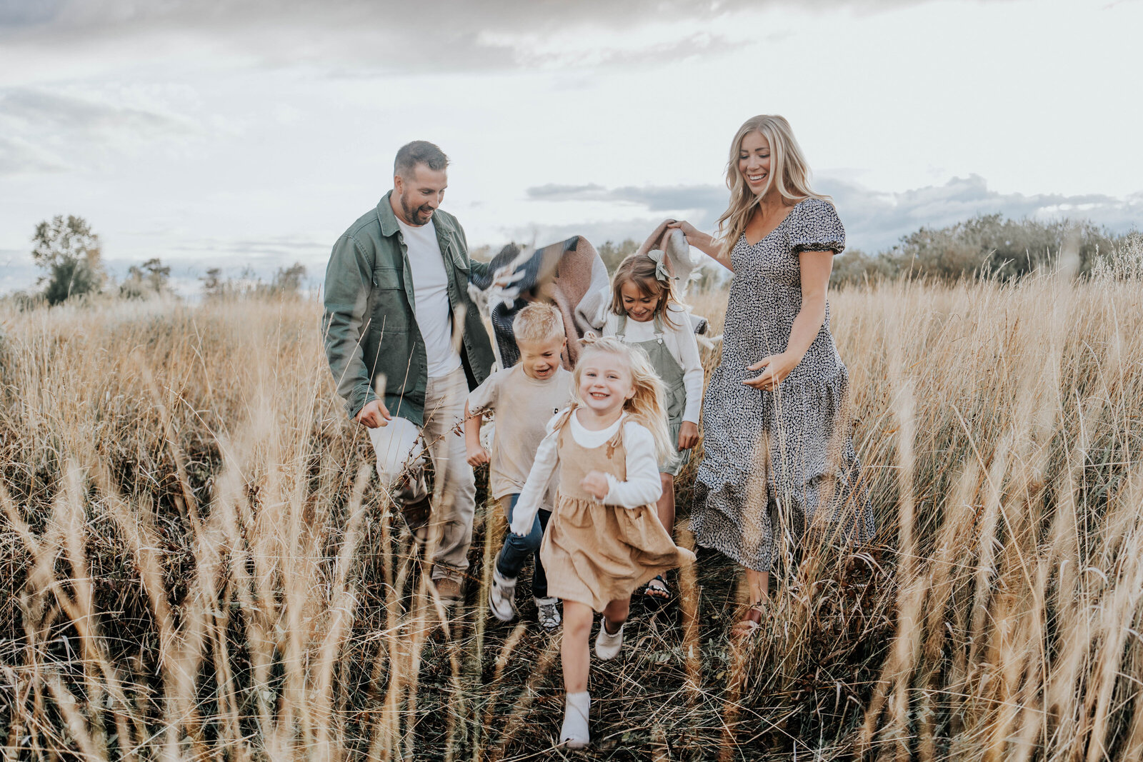 family laughing and playing in a wheat field surrounded by the golden hue of the sun captured by a Idaho Falls Family Photographer
