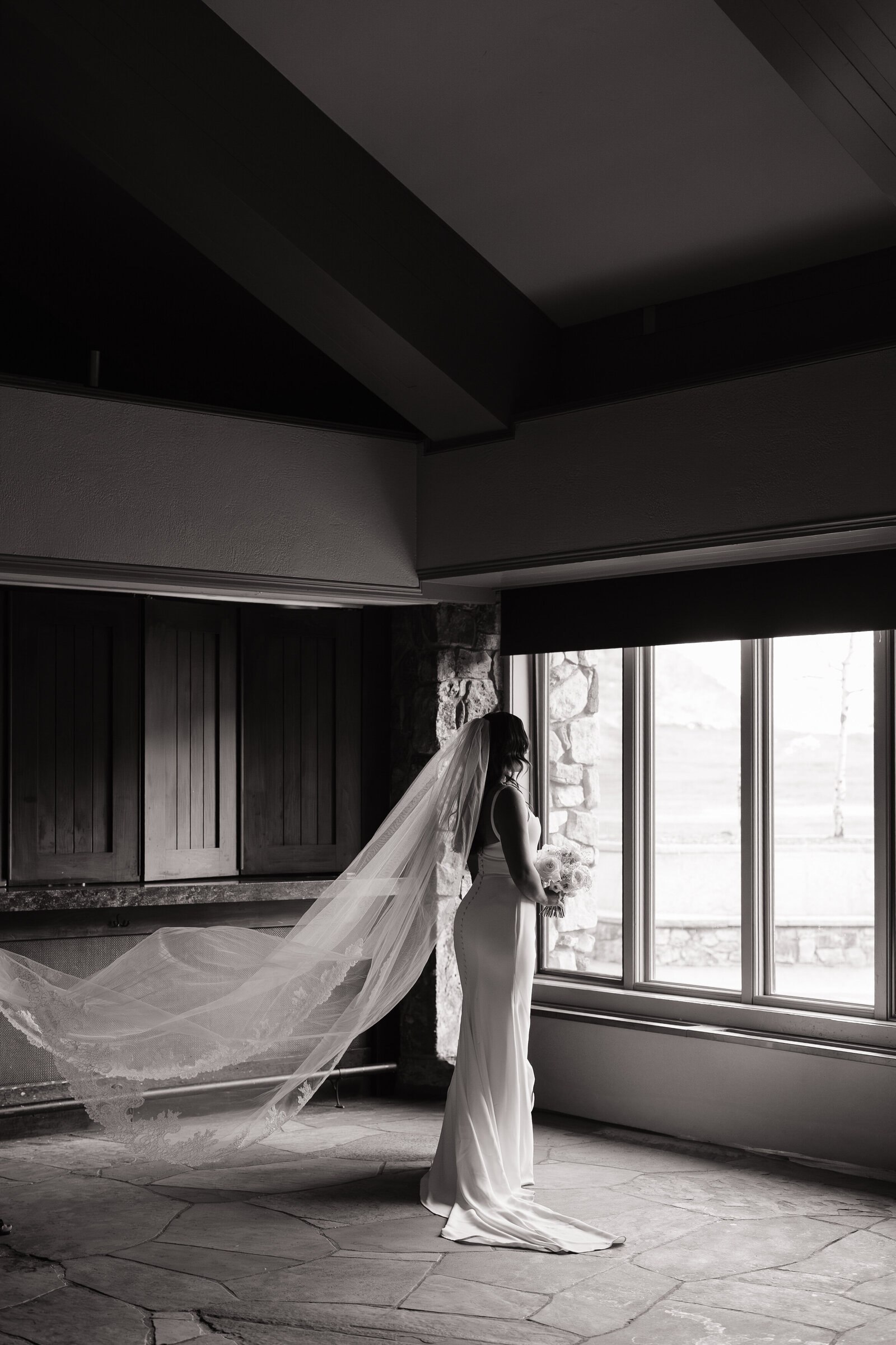Bride poses with flowing veil in front of windows by Ketchum elopement photographer