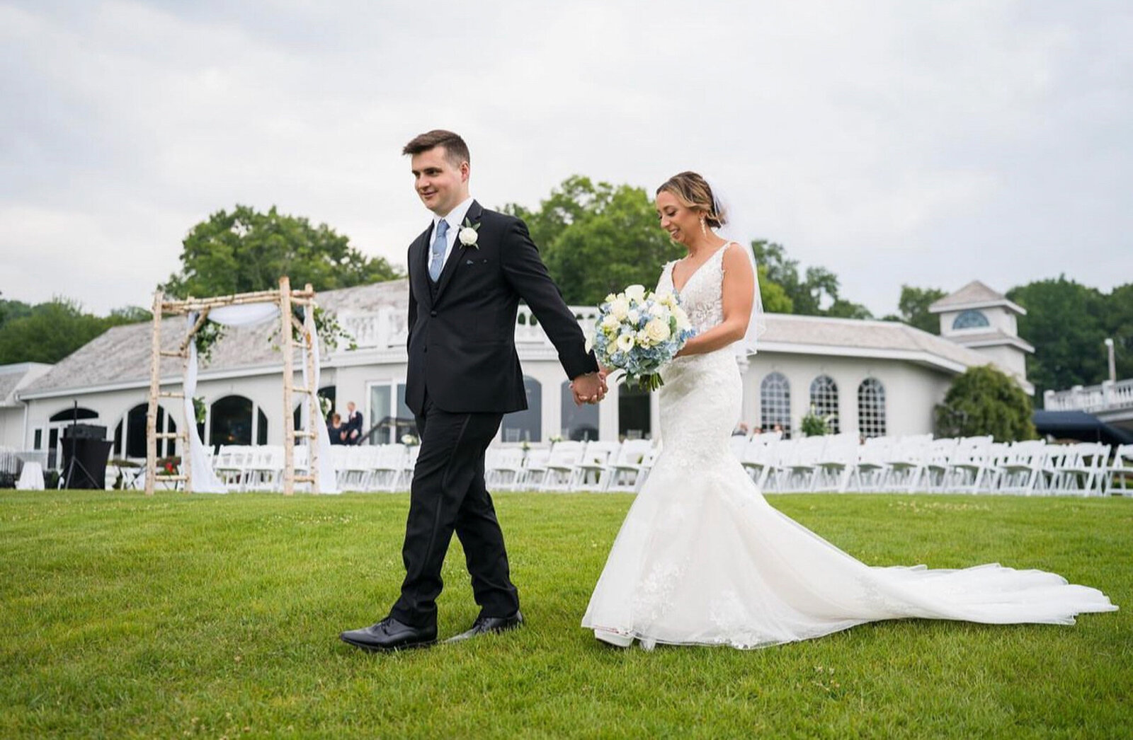 bride and groom walking on a grassy lawn while holding each other's hand