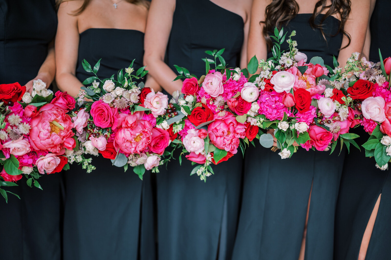 Close up image of black bridesmaid dresses and their colorful pink and red bouquets