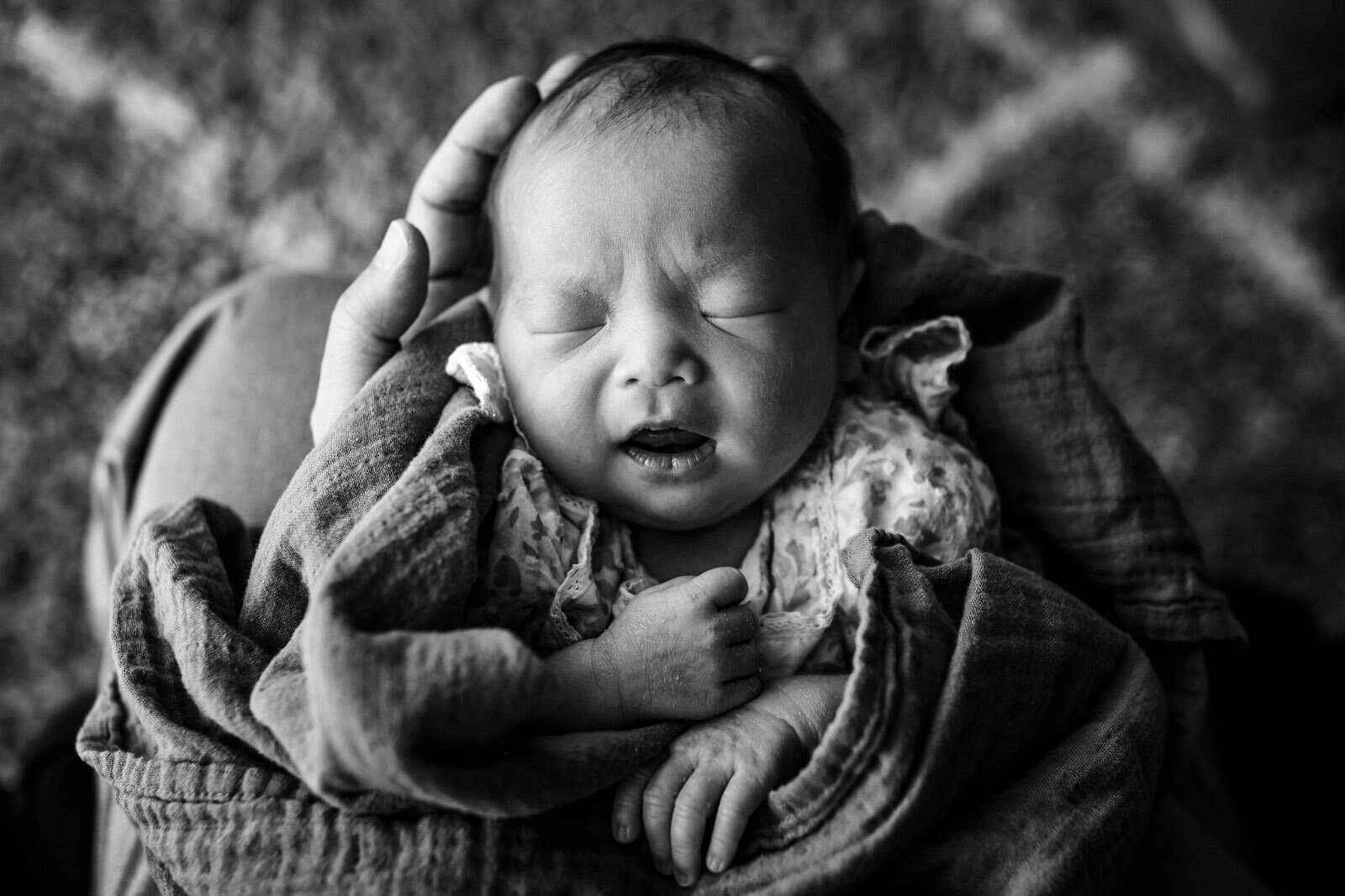 newborn with eyes closed and mouth open sleeping in Dad's lap with her head in his hands