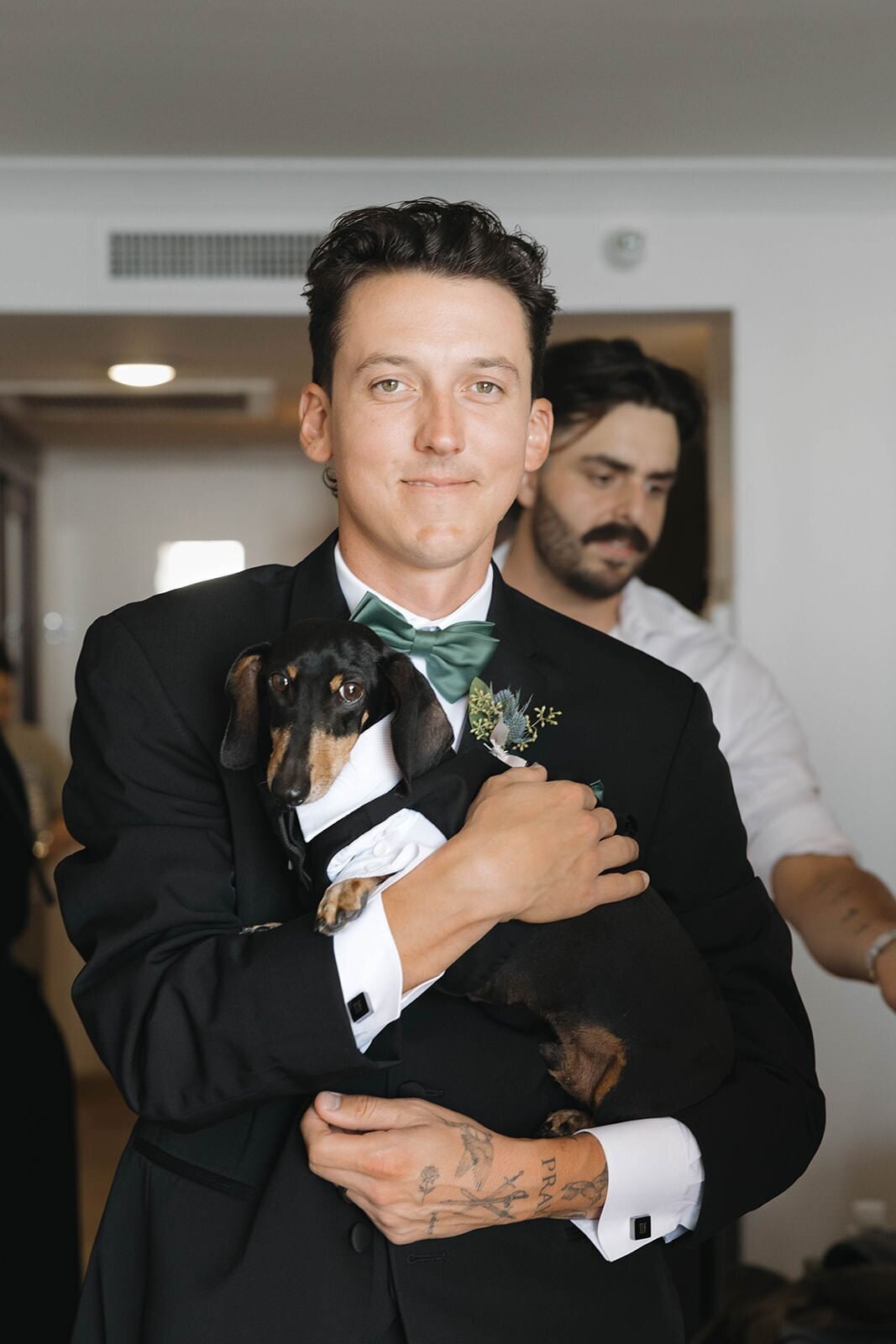Groom smiling and holding his dachshund in a tux