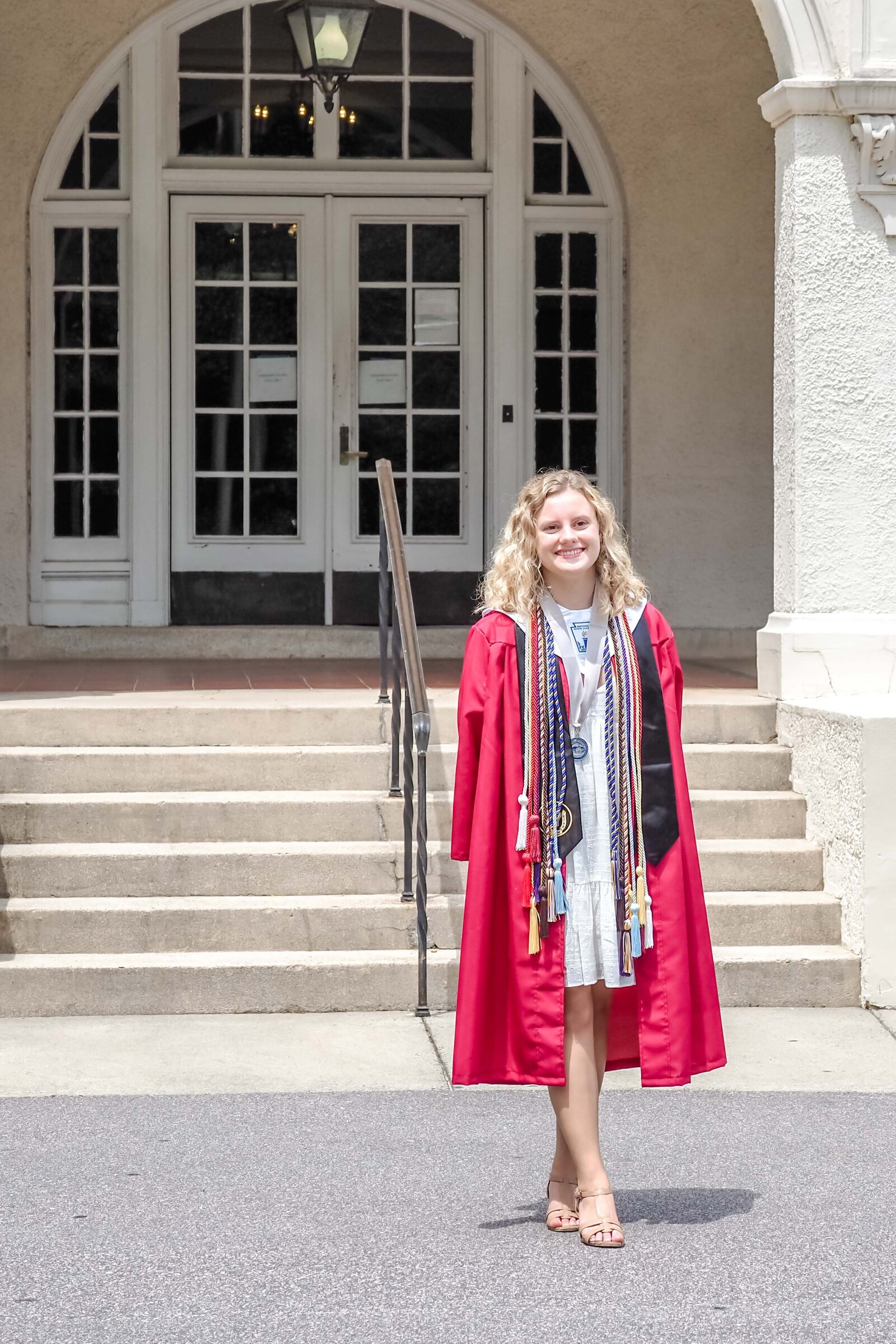 A NCSSM senior in a red graduation gown with honor cords standing on the steps of a school building in North Carolina. This dignified image captures academic achievement, perfect for professional senior portraits.