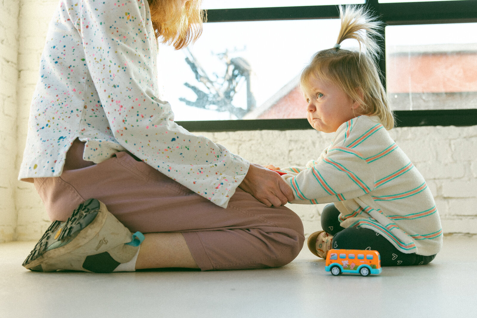 toddler girl with a sad face sitting on floor facing mom who is kneeling in front of her