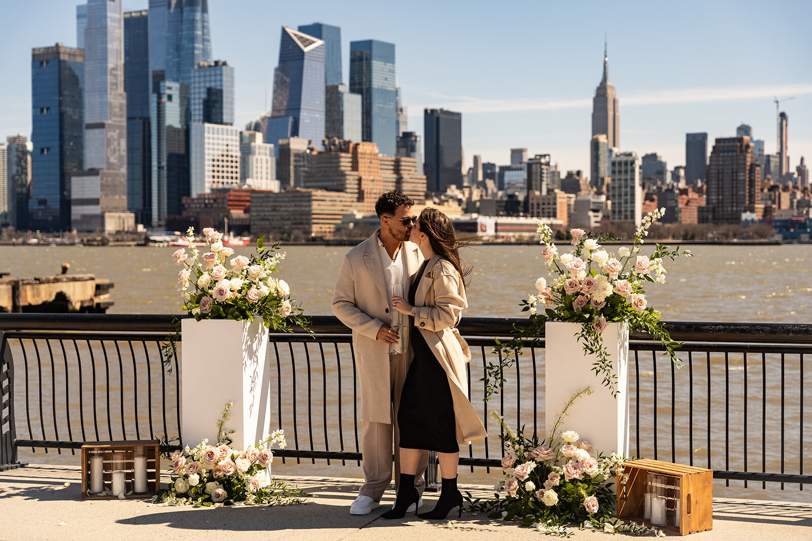Couple sharing a kiss during a romantic proposal setup with floral arrangements overlooking the New York City skyline, styled by Yours Truly, a wedding planner and designer in New Jersey.