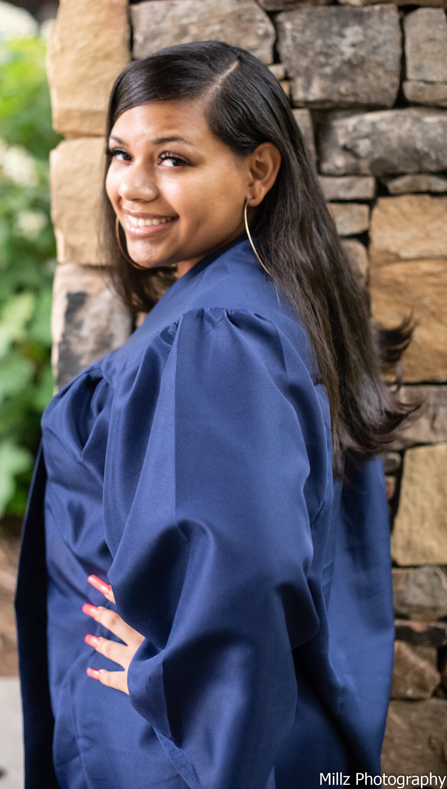 a senior dressed in her blue graduation gown smiling at the camera photographed by Millz Photography in Greenville, SC
