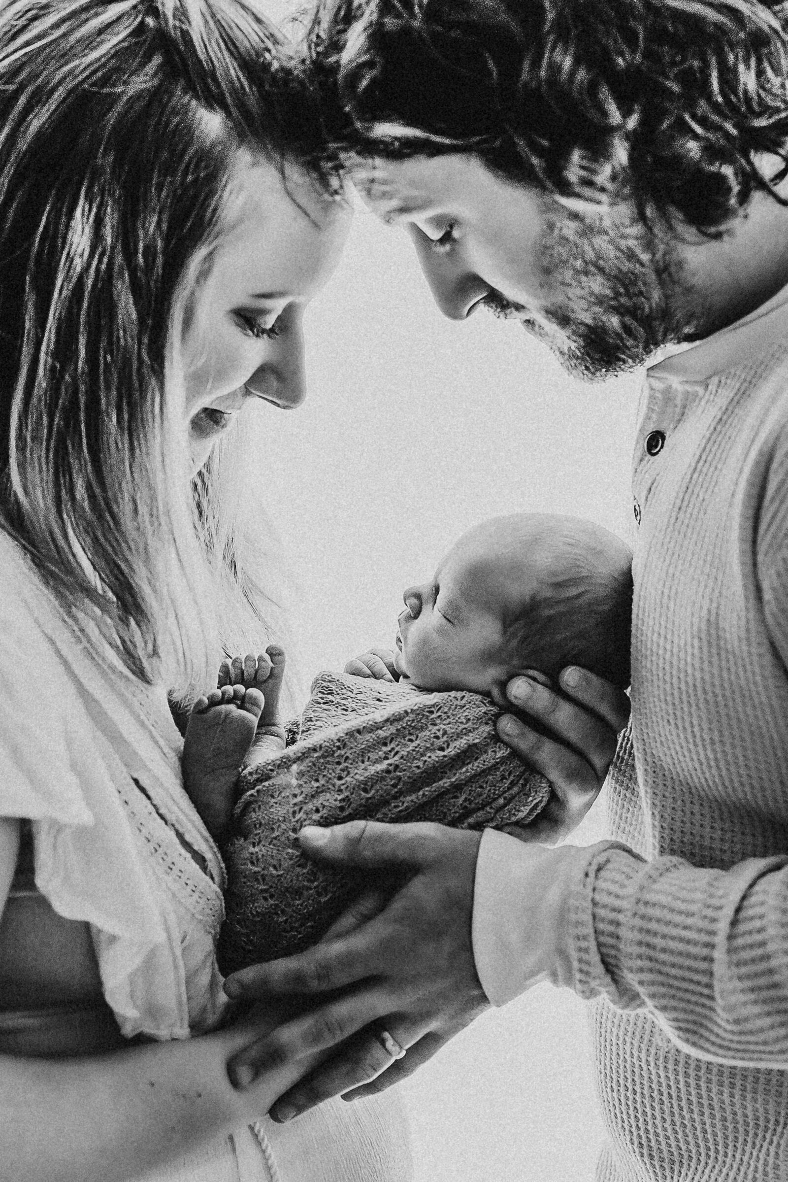 Newborn baby being held while his parents touch foreheads in window light in Upper Township, New Jersey